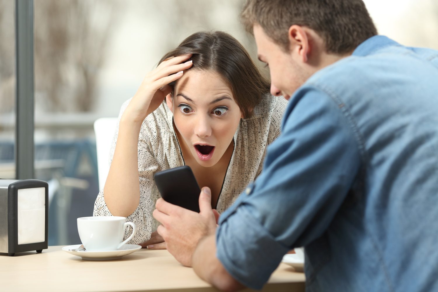 Surprised couple meeting in a coffee shop watching media content in a smart phone