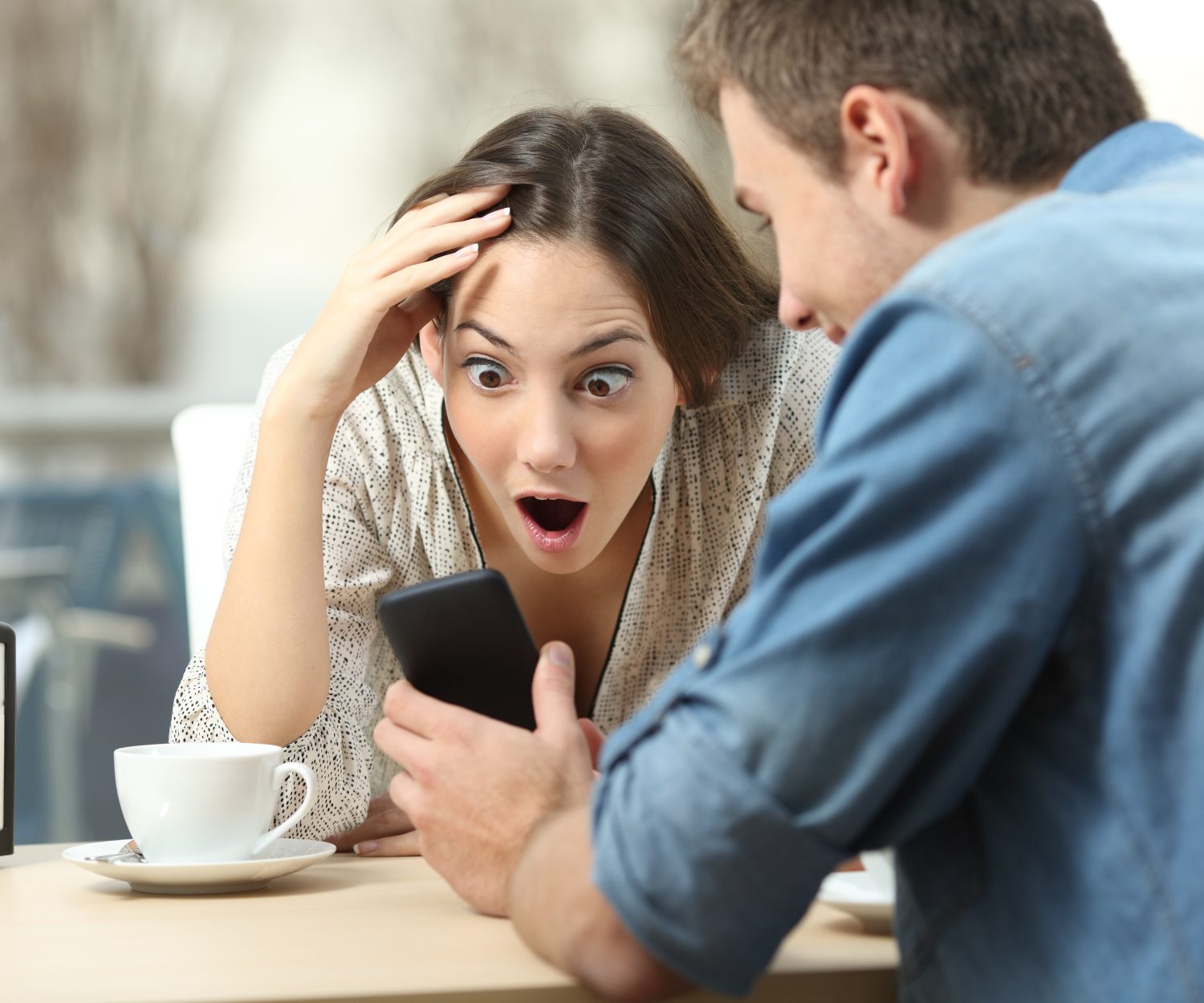 Surprised couple meeting in a coffee shop watching media content in a smart phone